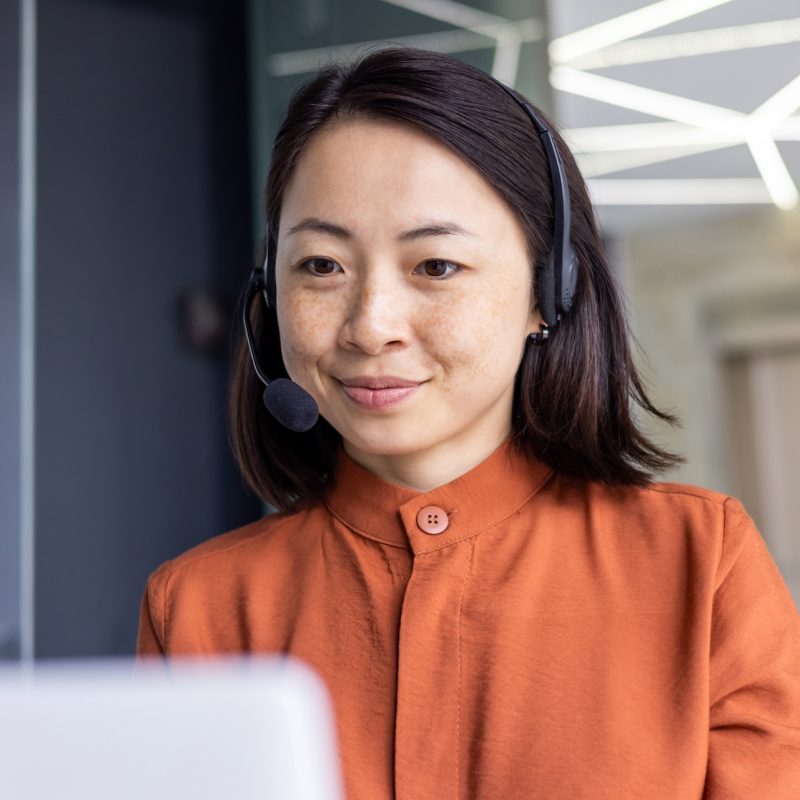 Serious Asian woman listening online conversation close up, businesswoman with headset phone, online customer support worker, working with laptop, video call consultation.